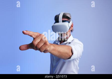 Mature businessman interacting with the metaverse while wearing virtual reality goggles. Senior businessman using his finger to press a virtual button Stock Photo