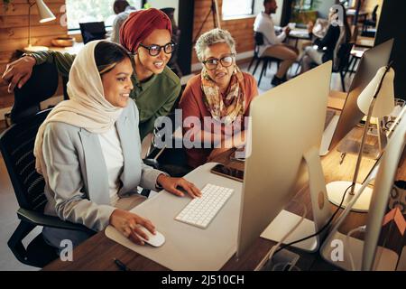 Happy businesswomen working as a team in a modern co-working office. Group of multicultural businesswomen having a discussion while looking at a compu Stock Photo