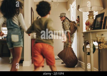 Happy military mom returning home to her children after deployment. Cheerful female soldier smiling with joy while receiving a warm welcome from her c Stock Photo