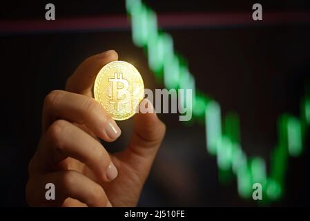 Bitcoin cryptocurrency coin in female hands against the graphs, rates on blurred background. Stock Photo