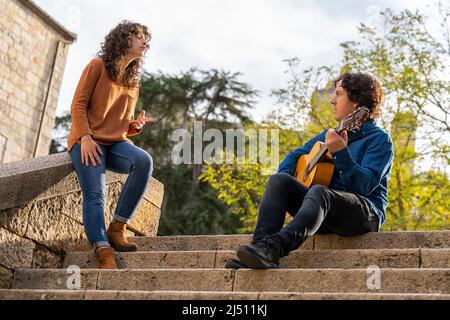 Young curly woman singing with a guitarist man in the street Stock Photo