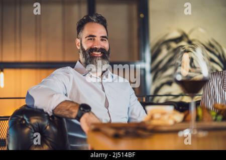 Happy adult man is sitting at restaurant, having dinner and wine. Stock Photo