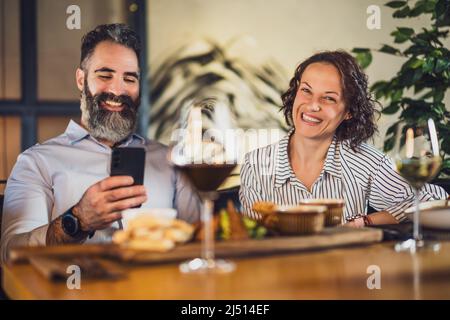 Happy couple is sitting at restaurant. They are having dinner with wine and spending nice time together. Stock Photo