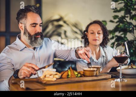 Adult couple is sitting at restaurant. They are having dinner with wine and spending nice time together. Stock Photo