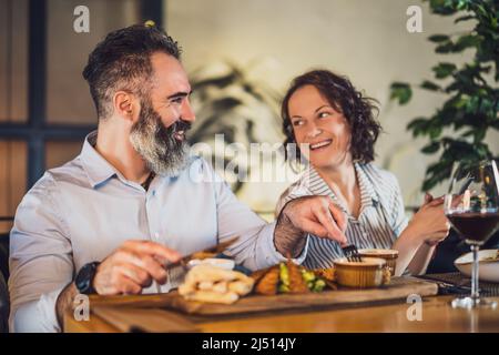 Happy couple is sitting at restaurant. They are having dinner with wine and spending nice time together. Stock Photo
