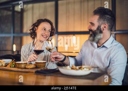 Happy couple is sitting at restaurant. They are having dinner with wine and spending nice time together. Stock Photo