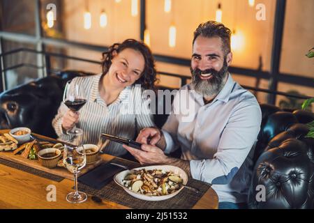 Happy couple is sitting at restaurant. They are having dinner with wine and spending nice time together. Stock Photo