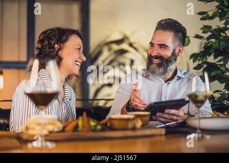 Happy couple is sitting at restaurant. They are having dinner with wine and spending nice time together. Stock Photo