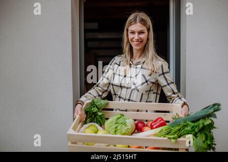 Woman holding delivered crate with vegetales and fruit from local farmer, sustainable lifestyle concept. Stock Photo