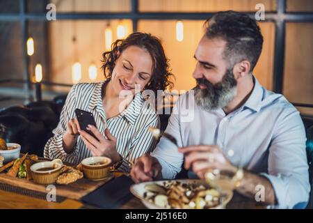 Adult couple is sitting at restaurant. They are having dinner with wine and spending nice time together. Stock Photo