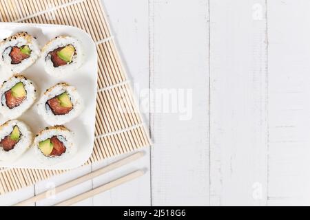 Sushi inside out rolls with salmon, avocado and sesame on side of wooden table Stock Photo