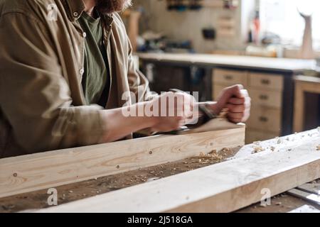 Professional male carpenter working in workshop using hand plane to smooth wooden plank surface Stock Photo