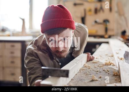 Portrait of bearded male carpenter using steel square while working with wood plank in woodshop Stock Photo
