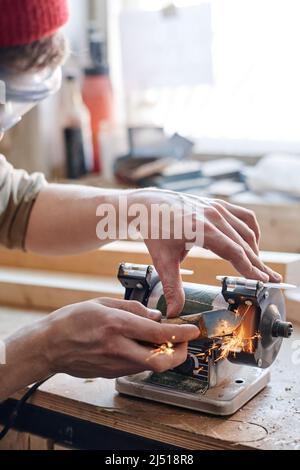 Close-up of unrecognizable man working in woodworking workshop sharpening knife using grinding jig Stock Photo