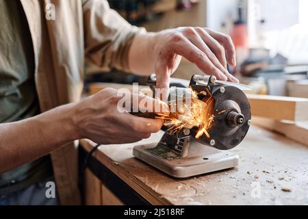 Medium close-up of professional carpenter working in joinery workshop sharpening knife using grinding jig Stock Photo