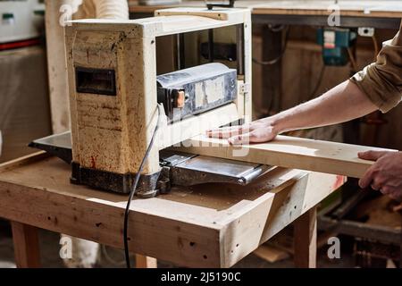 Unrecognizable male carpenter working using thickness planer machine to trim wood plank in woodworking workshop Stock Photo