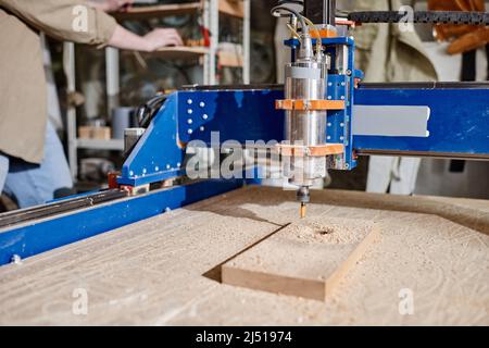 Unrecognizable carpenter operating CNC milling machine to make holes in wooden block, medium close-up shot Stock Photo