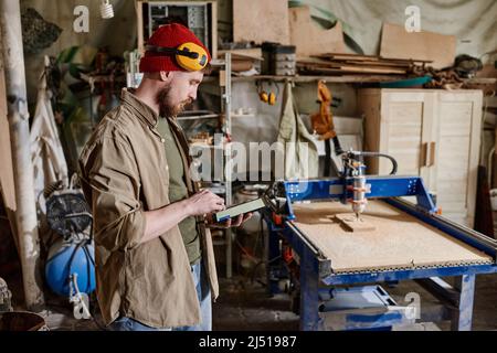 Modern professional carpenter standing in woodworking workshop using digital tablet to do calculations Stock Photo