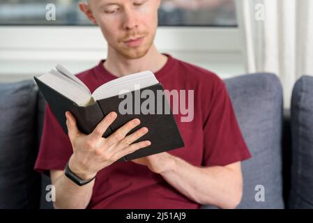 Bald hairless man reading book sitting on couch Stock Photo