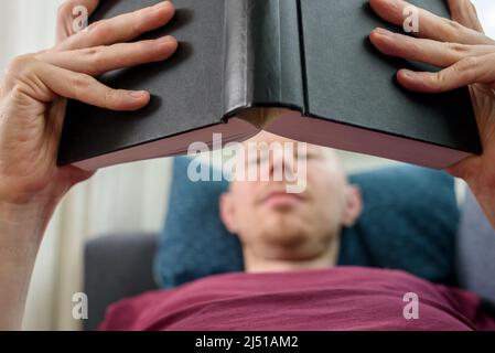 Bald hairless man reading book lying on couch Stock Photo