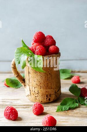 Raspberries in the corkwood cup on the wooden table with leaves Stock Photo