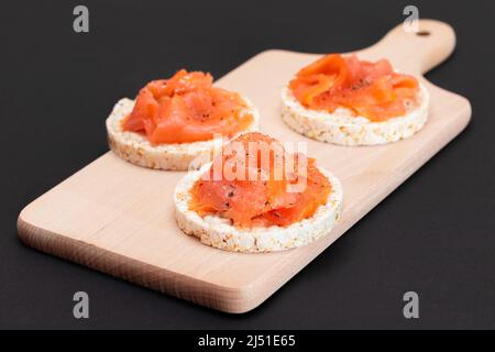 Tasty Rice Cake Sandwiches with Fresh Salmon Slices on Wooden Cutting Board. Easy Breakfast and Diet Food. Crispbread with Red Fish. Healthy Dietary Snack Stock Photo