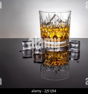 Glass of whisky with ice, backlit on a reflective black foreground in a cut glass tumbler. Stock Photo