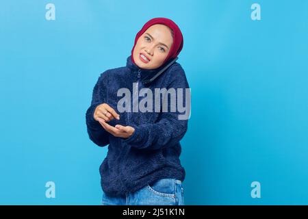 Portrait of young woman talking on cell phone while gesturing writing on blue background Stock Photo