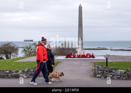 Couple with dog walking past the War Memorial at the seafront in the County Down coastal village of Groomsport, Northern Ireland. Stock Photo