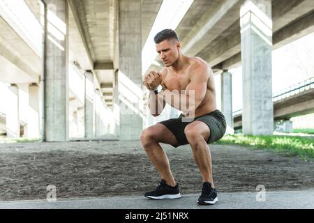 Young and muscular man is doing squats under the bridge during his street workout Stock Photo