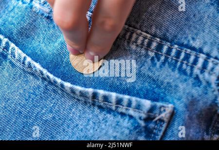 hand puts gold coin change in jeans pocket money concept  Stock Photo