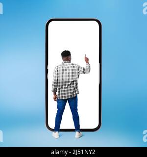African Man Using Huge Smartphone Over Blue Background, Rear View Stock Photo