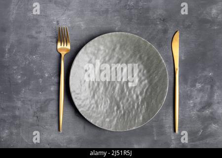 Empty grey textured plate and golden cutlery fork and knife on grey wooden background. Mock up for prepared dish, recipe or text. Minimal cooking imag Stock Photo