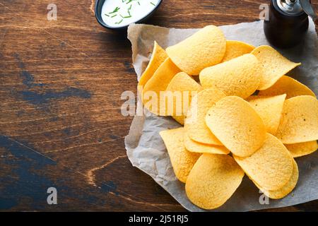 Potato corrugatedchips. Fast food. Crispy potato chips ceramic black bowl with sour cream sauce and onions in wooden stand on old kitchen table wooden Stock Photo