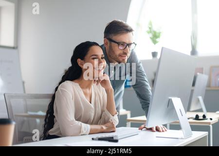 Smiling male and female employees discussing business project, using computer at company office, copy space Stock Photo