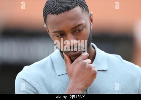 Front view portrait of a worried man with black skin thinking in the street Stock Photo