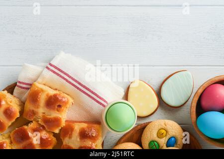 Easter hot cross buns with colored eggs, Easter gingerbread rabbits and cookies over white plank wooden old table background . Spring holiday baking c Stock Photo