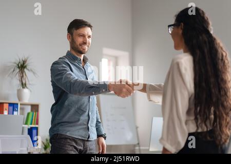 Happy businessman shaking hands with young businesswoman at office. HR manager welcoming job applicant into company team Stock Photo