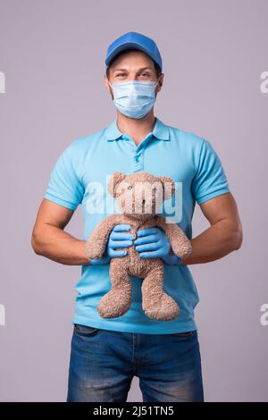 Young Delivery Man With A Teddy Bear Is Wearing Prevention Mask And 