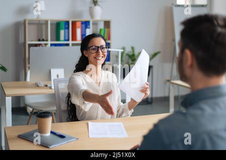 Happy HR manager holding CV, offering handshake to job applicant during employment interview at modern office Stock Photo