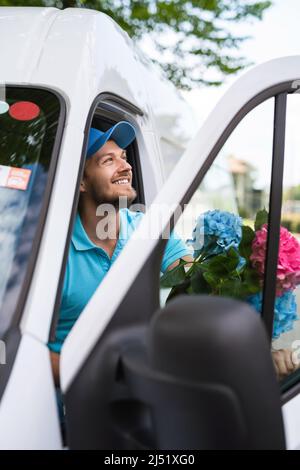 Happy courier inside the white van during flowers delivery is waiting for a client Stock Photo