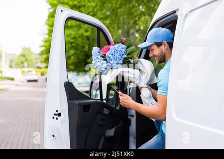 Happy courier inside the white van during flowers delivery is waiting for a client Stock Photo