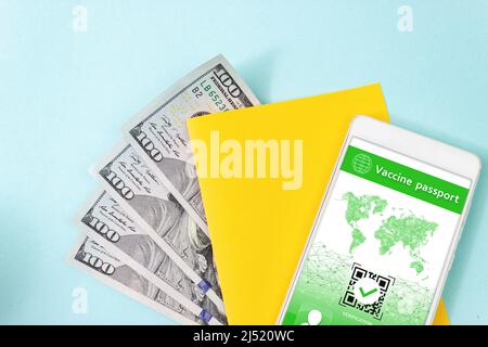 Close up blank yellow piece of paper, 100 dollar bills and smartphone displaying valid digital vaccination certificate QR Code for COVID-19 Stock Photo