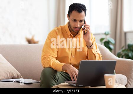 Focused Arab man working and talking on phone at home Stock Photo