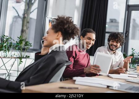 Cheerful multiethnic businessmen using digital tablet while african american colleague talking on smartphone in office Stock Photo