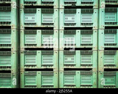 Stack of green color old and damaged used plastic packaging crates background. Stock Photo