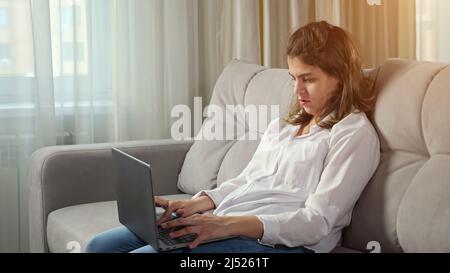 Disabled woman works on computer sitting on sofa at home Stock Photo