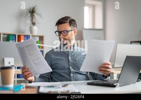 Focused mature engineer businessman in glasses working with documents, sitting at workplace in office interior Stock Photo