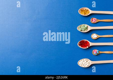 Top view Variety of vitamin and mineral pills in wooden spoon on Colored background. Top view of assorted pharmaceutical medicine pills. Dietary suppl Stock Photo