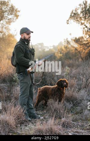 Young hunter standing and holding his shotgun in nature with his dog Stock Photo